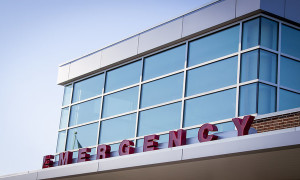 Emergency room entrance with red block letters on the metal awning of a hospital building, blue tone filter.