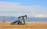 A Pump jack pumping oil from an oil well in the plains with snow capped mountains in the background.