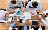 business, people, statistics and team work concept - close up of creative team with charts and gadgets meeting and drinking coffee in office