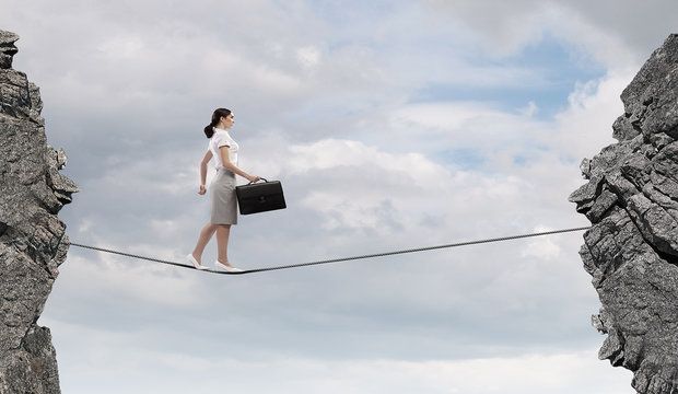 Young confident businesswoman walking on rope above gap