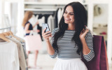 Technologies make shopping easier. Beautiful young woman with shopping bags using her smart phone with smile while standing at the clothing store