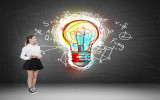 Woman standing near blackboard with giant colorful light bulb sketch pictured on it with formulas surrounding it. Concept of the next big thing