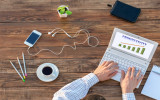 Natural Rough Wooden Desk Man Working Computer Top View Smart Casual Clothing Typing Keyboard with Productivity Chart on Screen Smart Phone and Cup of Coffee