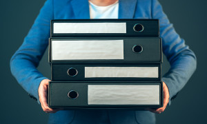 Accountant holding document binders with archived paperwork and other corporate legal sheets mock up copy space