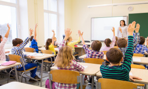 education, elementary school, learning and people concept - group of school kids with teacher sitting in classroom and raising hands