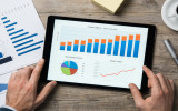 Top view of digital tablet with financial year overview on screen. Businessman analyzing investment charts with digital tablet on wooden desk at office. positive stock market trend.