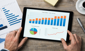 Top view of digital tablet with financial year overview on screen. Businessman analyzing investment charts with digital tablet on wooden desk at office. positive stock market trend.