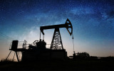 Silhouette of oil pump is pumping crude oil on the oil field in the night under sky with stars and Milky Way. Oil industry equipment