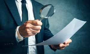 Tax inspector investigating financial documents through magnifying glass forensic accounting or financial forensics inspecting offshore company financial papers documents and reports.