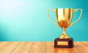 Golden trophy cup on wood table over blue wall. 3D illustration of sports award goblet