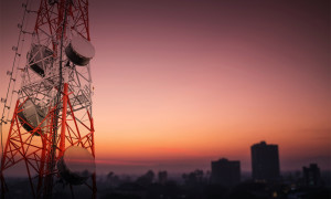 Telecommunications tower and satellite dish telecom network with silhouette of countryside area in sunrise