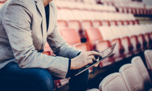 Young and successful football manager working on a tablet, and sitting on the stands alone. Cropped photo.