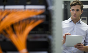 Computer technician using digital tablet performing maintenance check of mainframe equipment