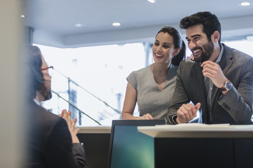 Smiling couple customers talking to receptionist at desk in car dealership