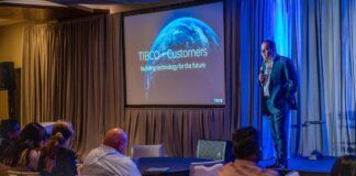 A man in a suit delivers a presentation at a conference, engaging the audience with his insights and expertise.
