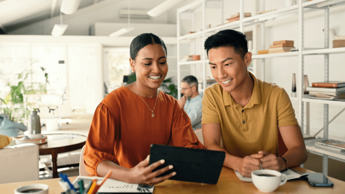 Two people sitting at a table with digital tablet and coffee cup in a modern workspace.