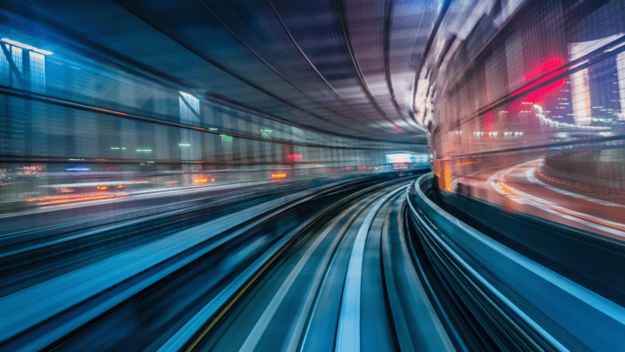 Blurred motion view of a cityscape from a moving train at night with vivid lights.