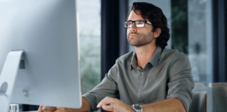 Man sitting at a desk using a computer with a white mouse.
