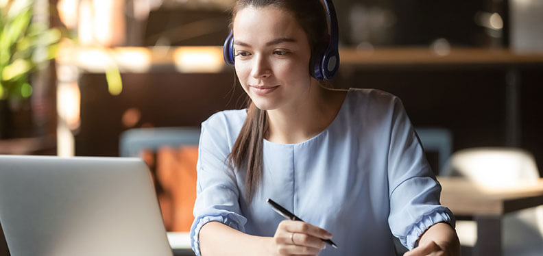 Woman wearing headphones looking at laptop while holding a pencil