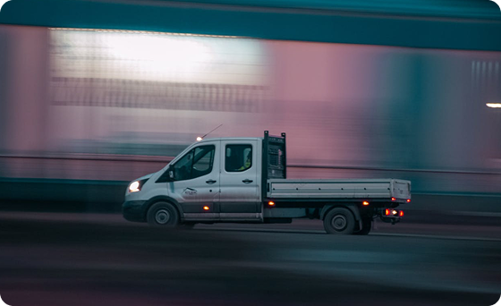 White flatbed truck driving on a road with motion blur in the background.